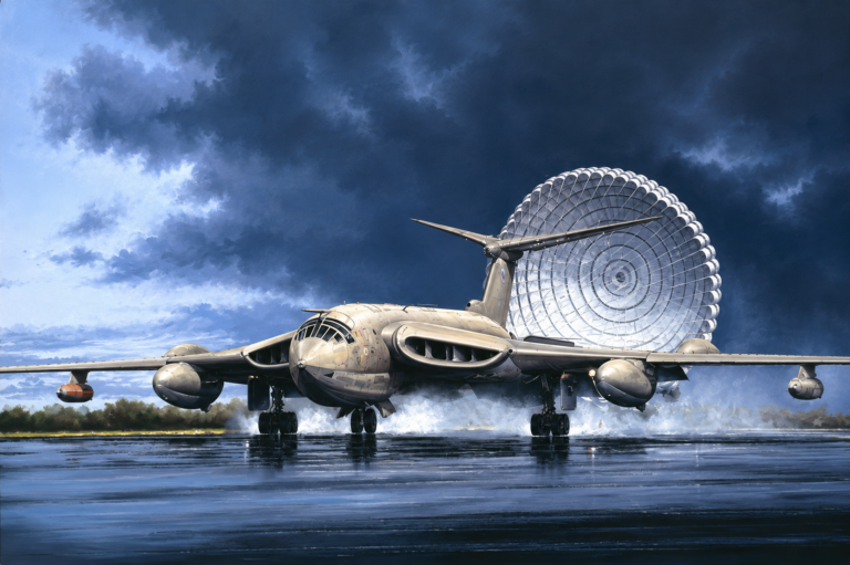 Military transport aircraft on a wet runway as a large circular parachute-like system unfolds behind the tail against a stormy sky.