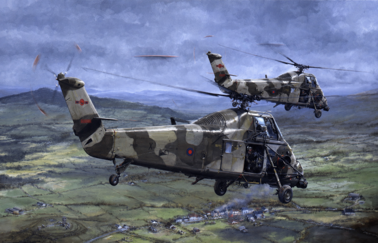 Two camouflaged RAF helicopters in a low pass over a green valley and small village below.