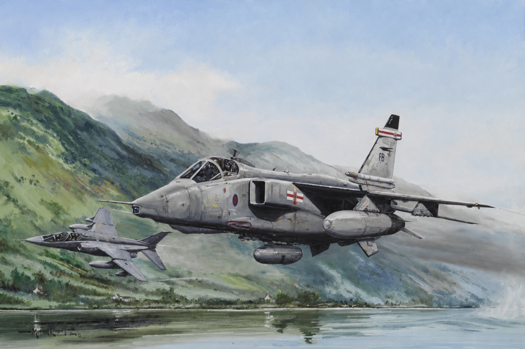 Two gray military jets fly in formation over a green, mountainous valley with a lake below and distant peaks in the background.