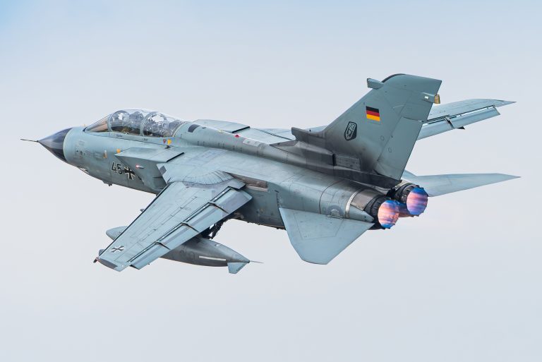 A high-resolution photograph by Kris Christiaens showing a German Air Force Panavia Tornado in a banking turn with afterburners glowing.