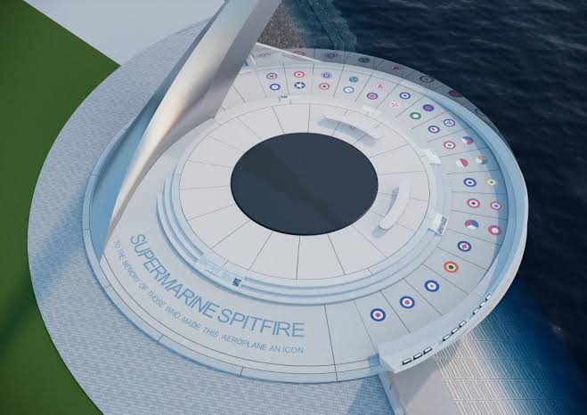 Circular white platform with a black central hub, labeled 'Supermarine Spitfire,' bordered by multiple colored roundels, set on a waterfront deck